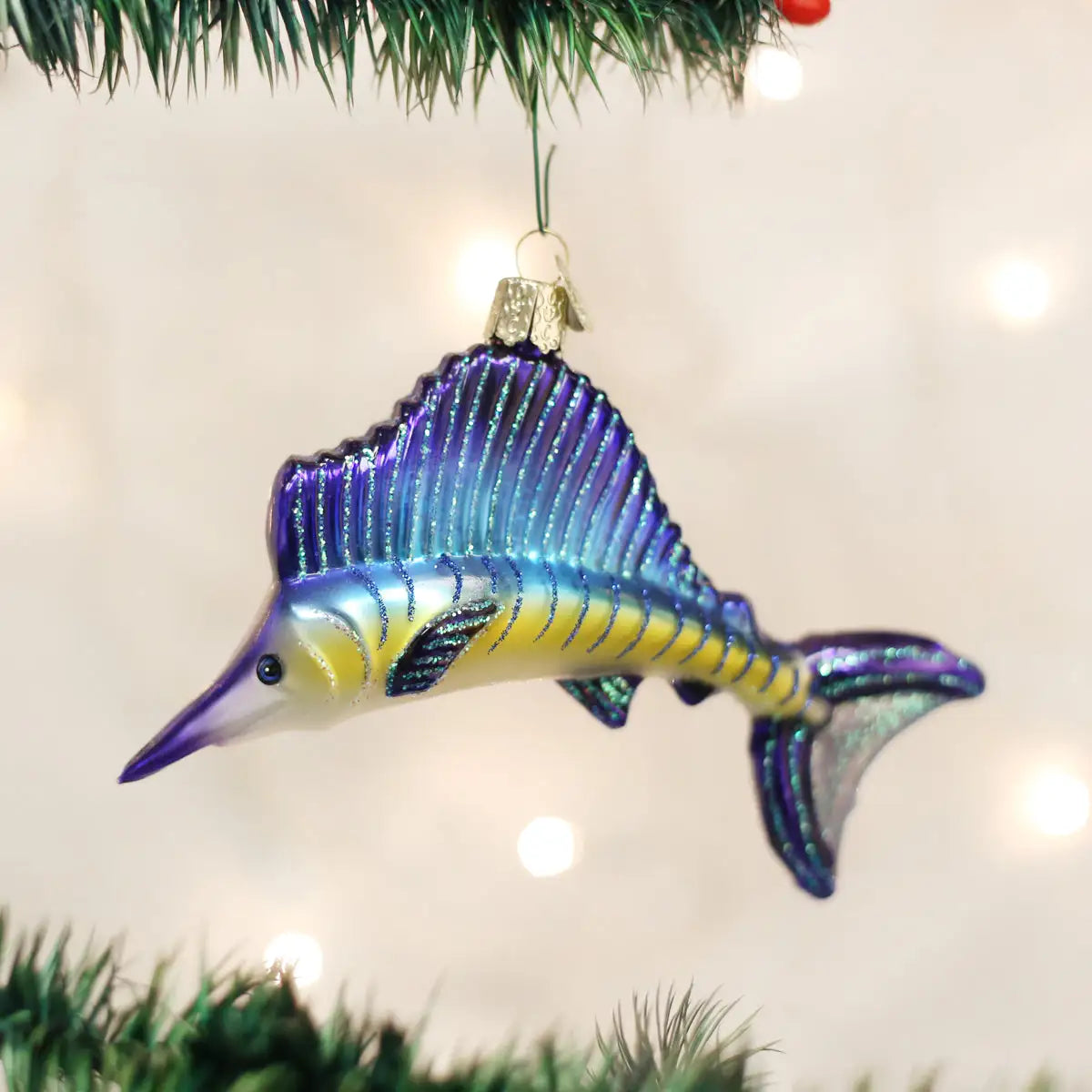 Decorative fish ornament hanging on a Christmas tree with lights in the background.