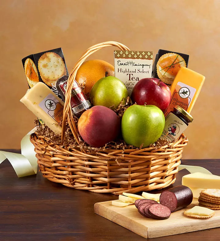 Wicker gift basket with fruits, cheese, and meats on a wooden table.