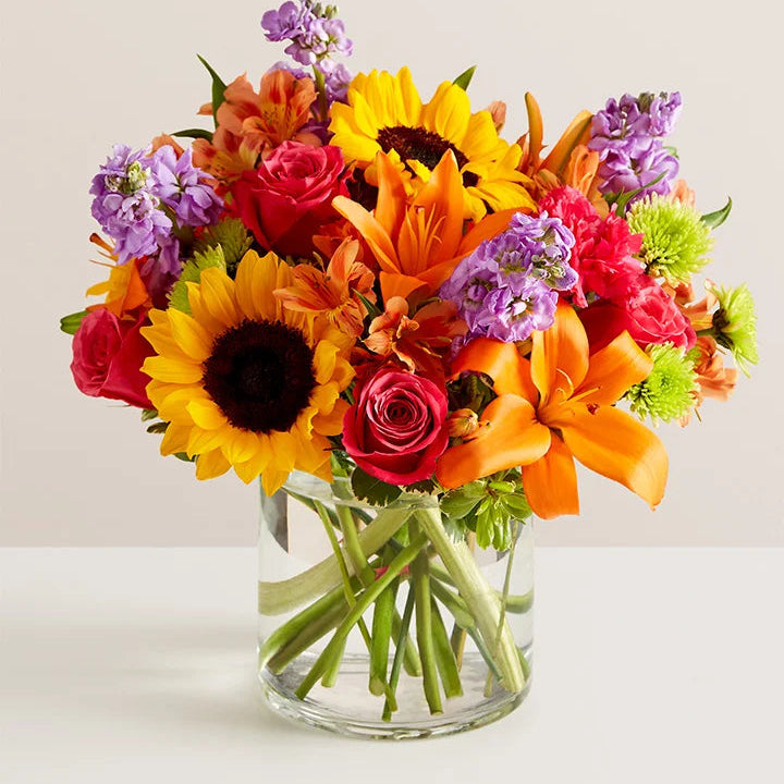 Bouquet of colorful flowers in a clear vase on a light background