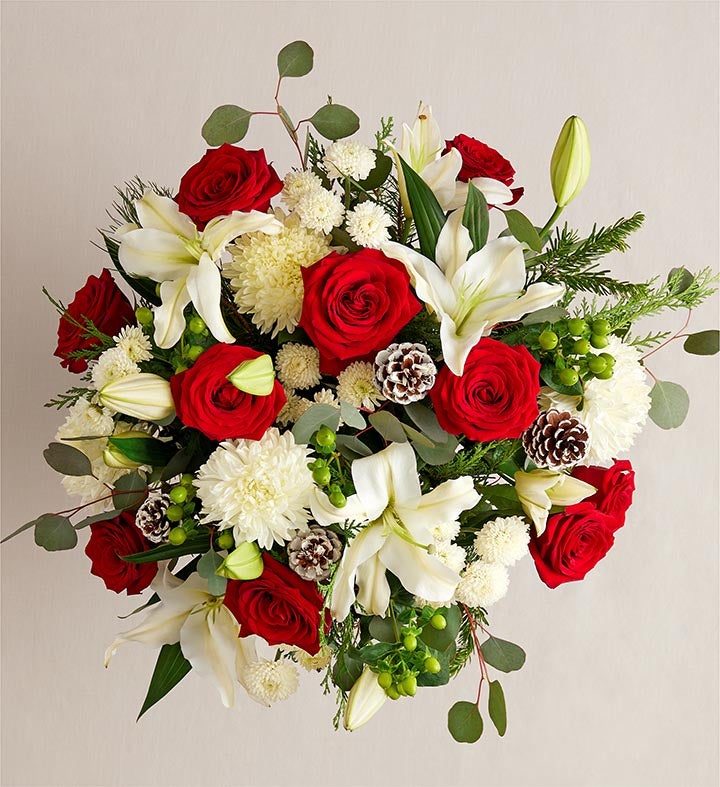 Bouquet of red roses and white lilies in a clear vase on a wooden surface with decorative items.