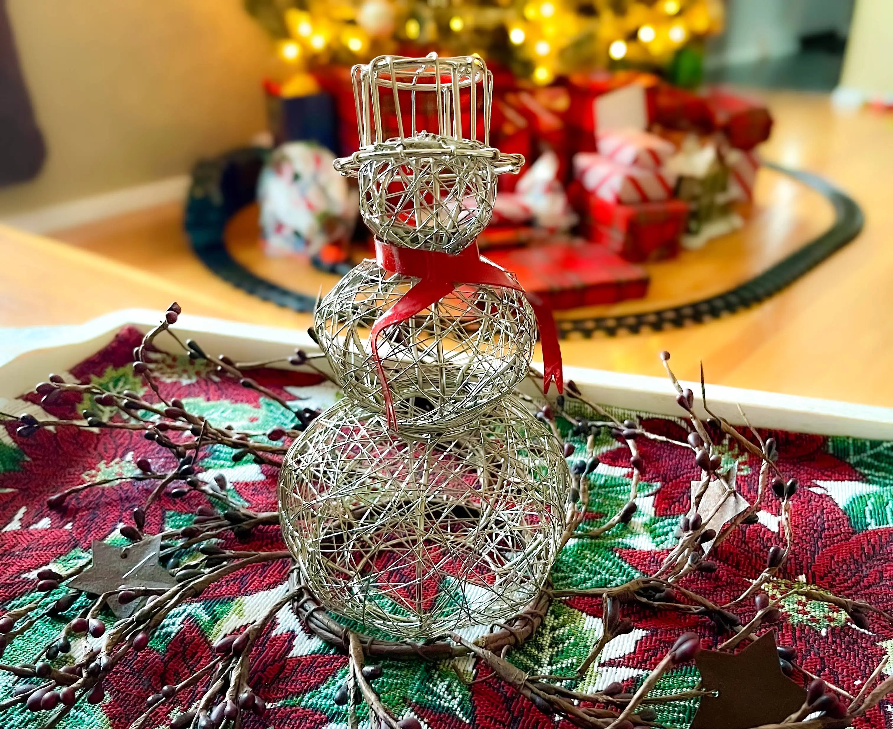 Decorative silver snowman ornament on a Christmas-themed tablecloth with blurred festive background.