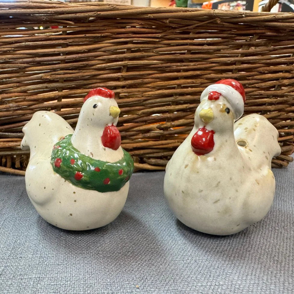 Two ceramic chickens with festive decorations in front of a woven basket.