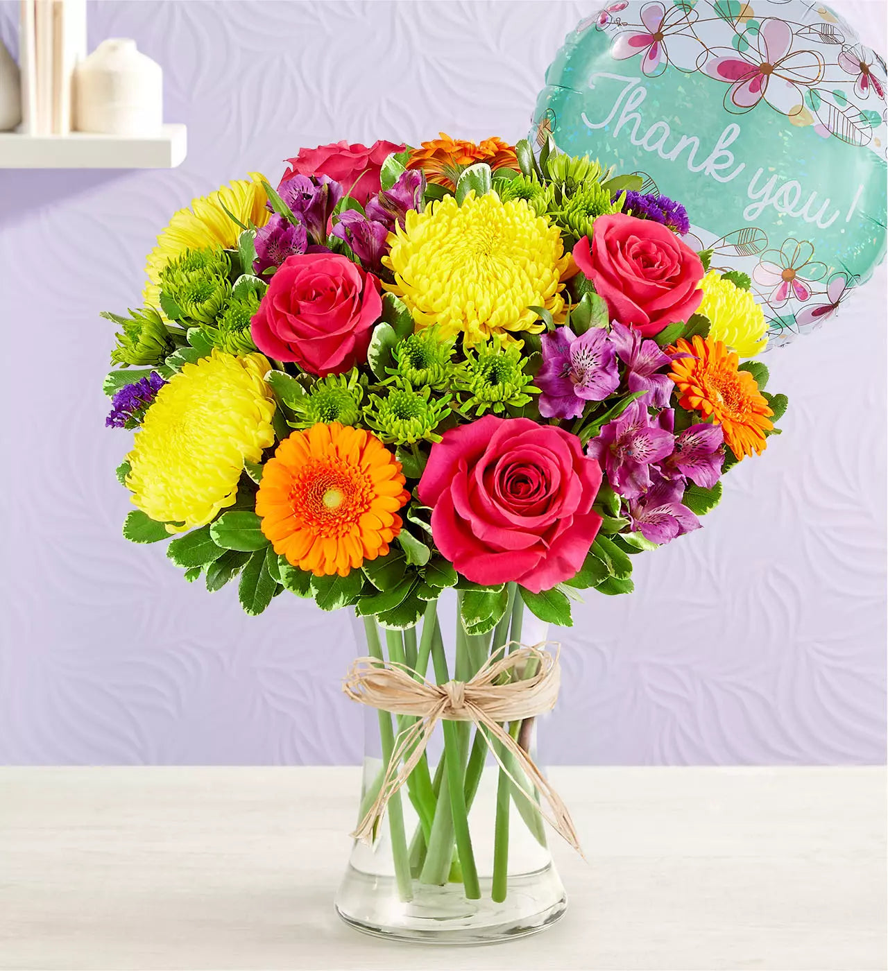 Colorful bouquet of flowers in a glass vase with a 'Thank you!' card on a light purple background.