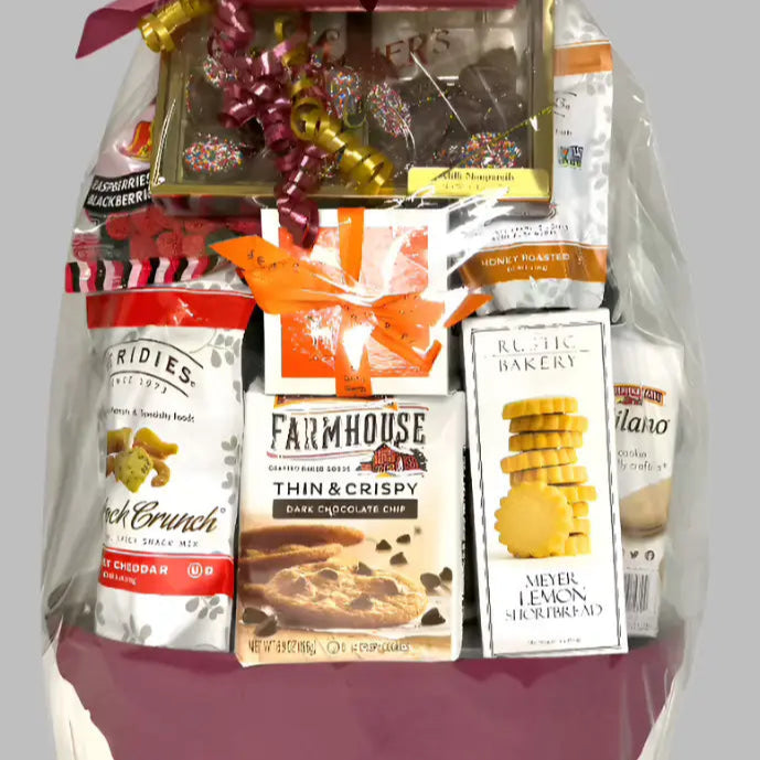 Gift basket with various products including snacks and a large red bow on a gray background