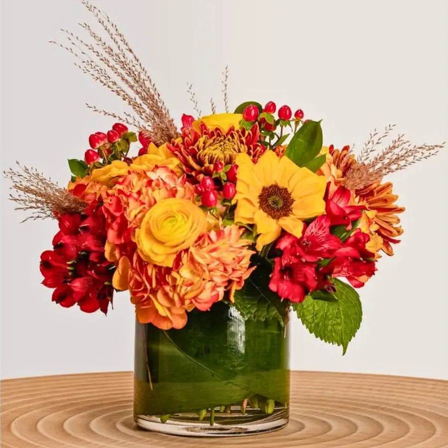 Colorful flower arrangement in a glass vase on a wooden surface with a light background