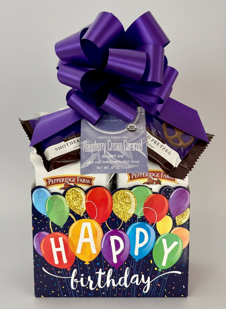 Gift basket with a purple bow, snacks, and 'Happy Birthday' packaging on a wooden surface.