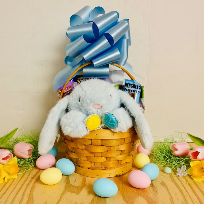 Gift basket with plush bunny, candy, and blue bow on a wooden surface.