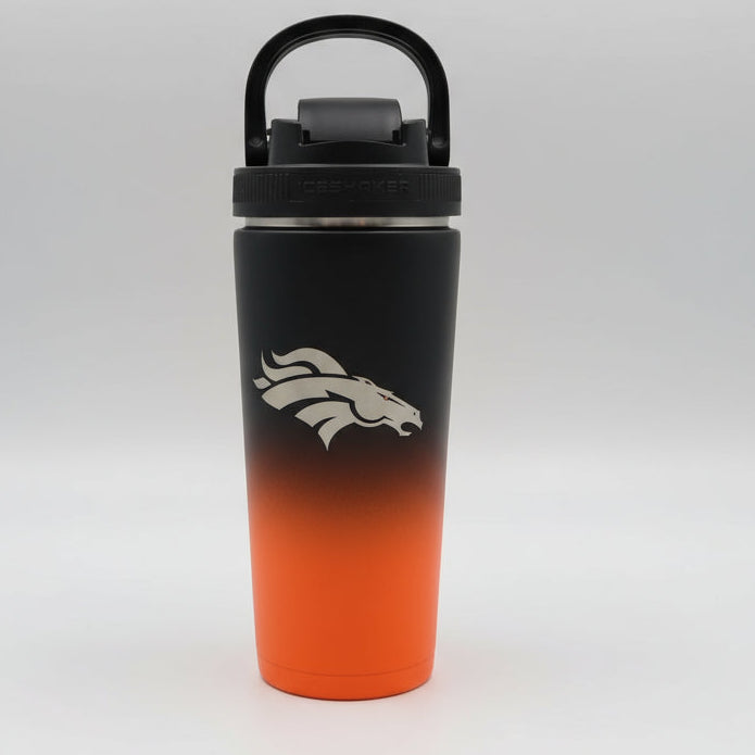 Black and orange tumbler with a logo on a wooden surface with greenery