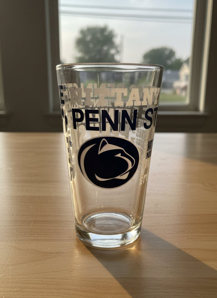 Clear glass with Penn State logo on a desk with papers and a phone.