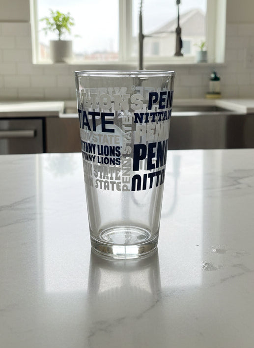 Clear glass with Penn State logo on a desk with papers and a phone.