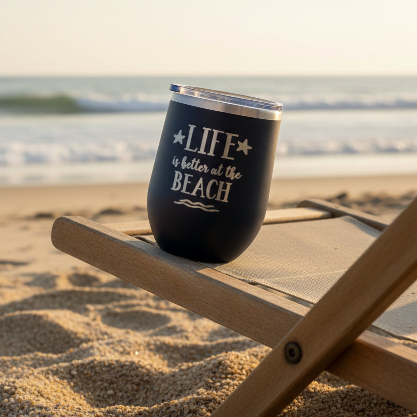 Black tumbler with 'Life is better at the Beach' text on a wooden surface.