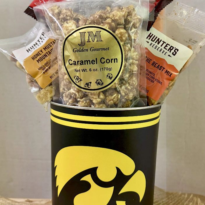 Snack basket with J&M Caramel Corn and other treats in a container with a logo on a wooden surface.