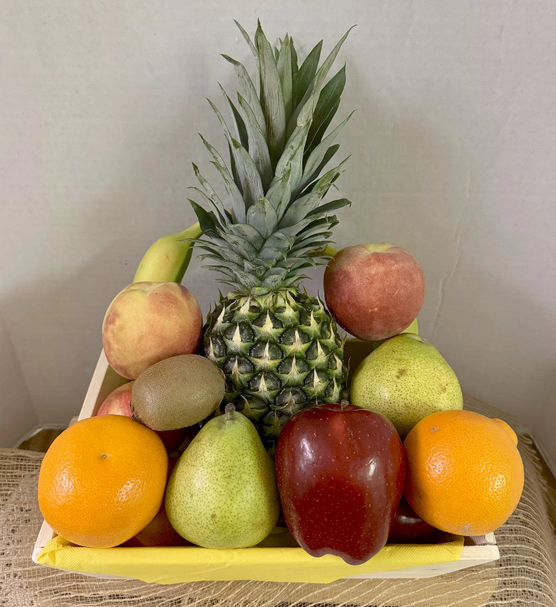 Assorted fruits including a pineapple, apples, oranges, and pears on a wooden tray.