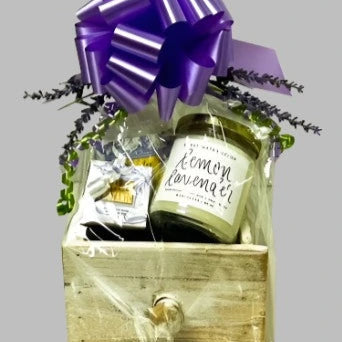 Gift basket with a purple bow, lemon lavender product, and other items on a gray background