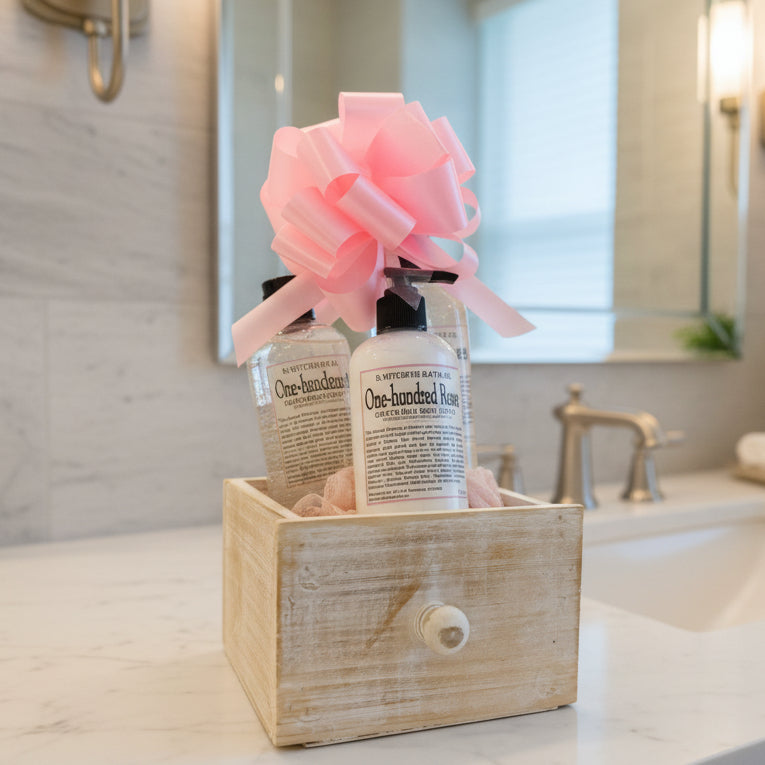 Two bottles of 'One Hundred Roses' bath oil in a wooden box with a pink bow on a light background.