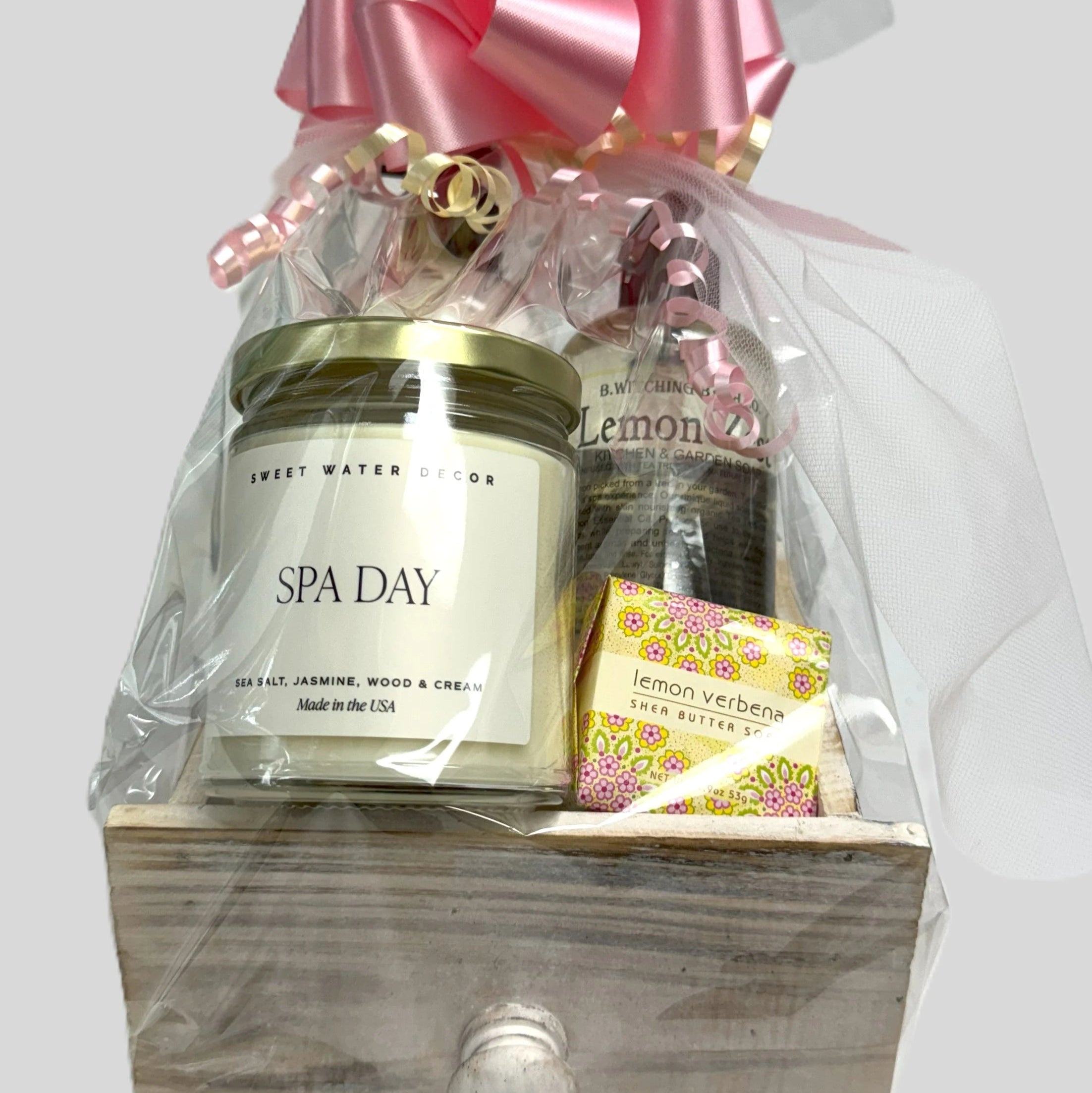 Gift basket with 'Spa Day' candle, bath bombs, and a pink bow on a white background