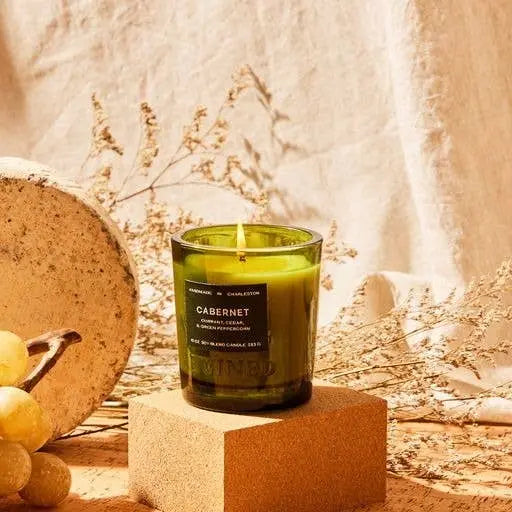 Green candle labeled 'CABERNET' on a wooden block with a neutral background