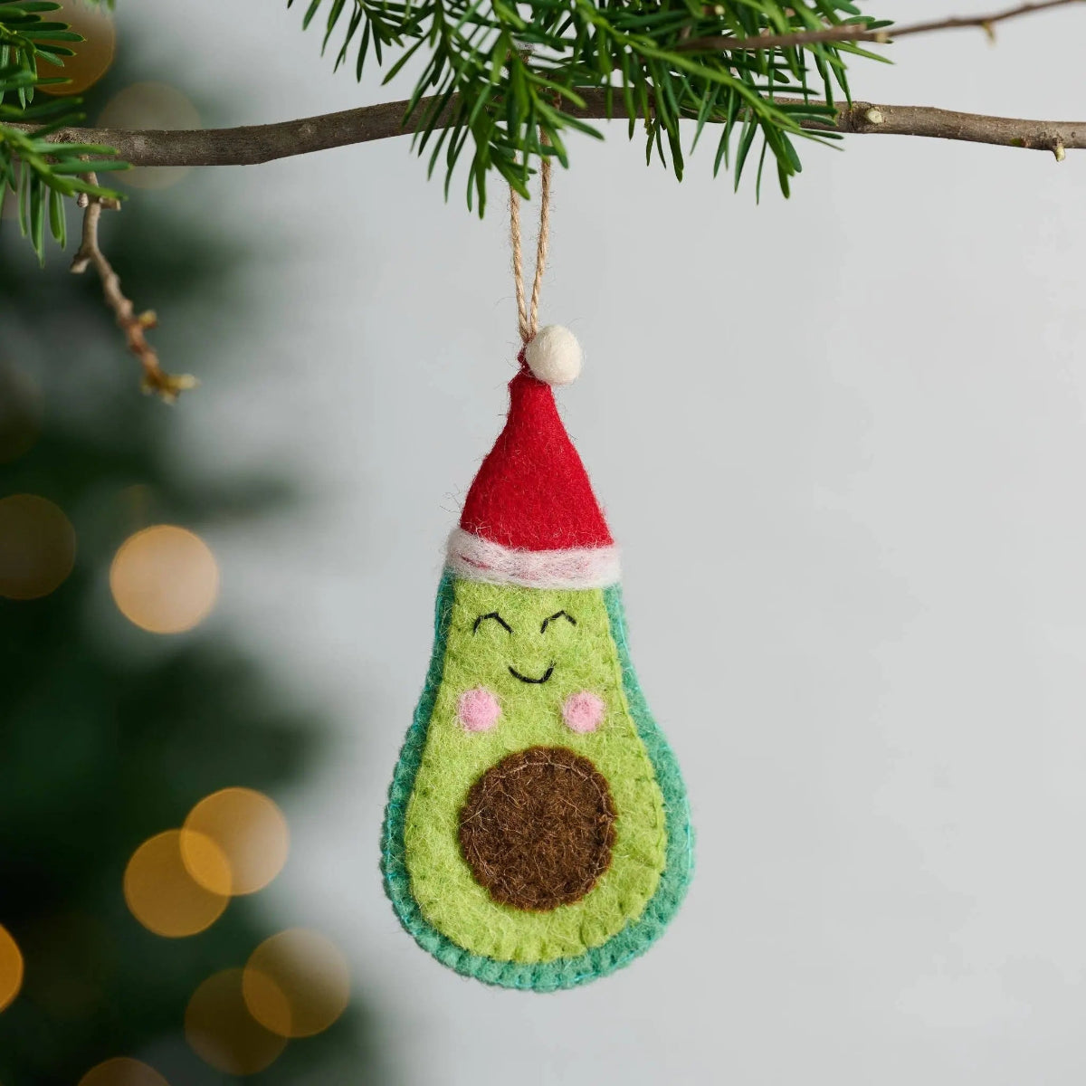 Avocado-shaped Christmas ornament with a red hat on a blurred green background