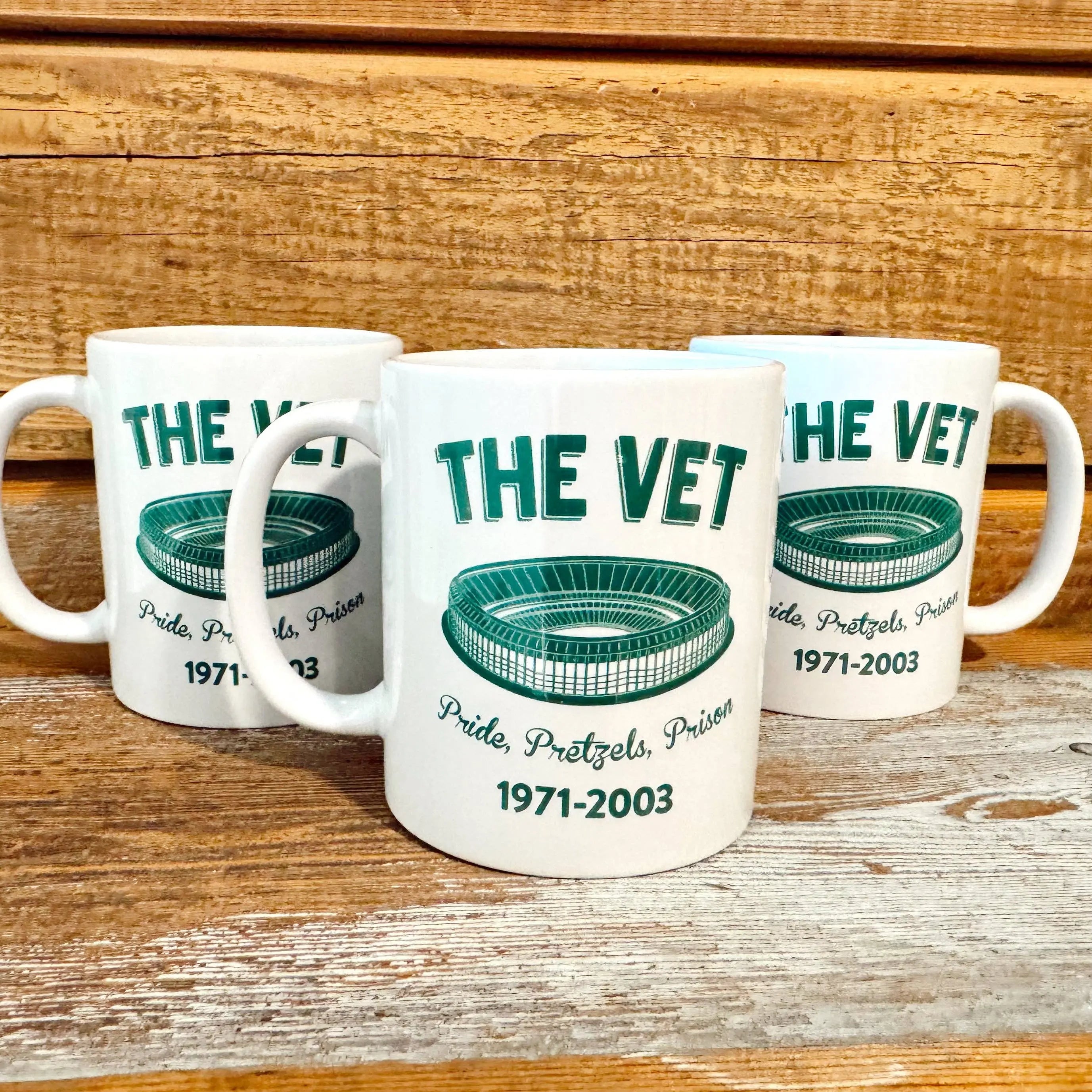 Three mugs with 'The Vet' stadium design on a wooden surface