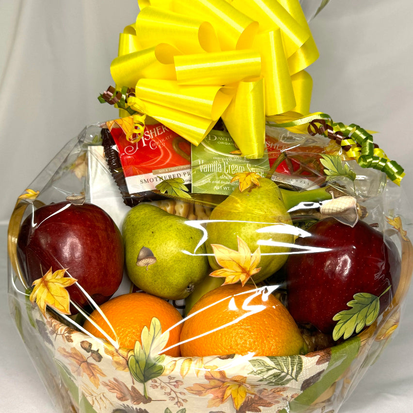 Fruit basket with apples, oranges, pears, and a small bag of chips on a wooden surface.
