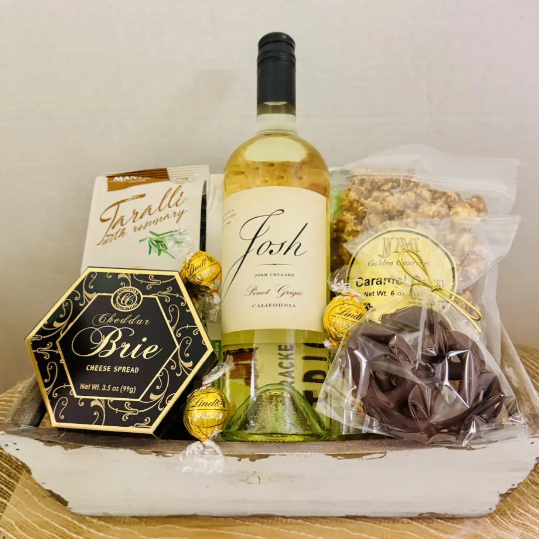 Gift basket with wine, cheese, and snacks on a wooden surface
