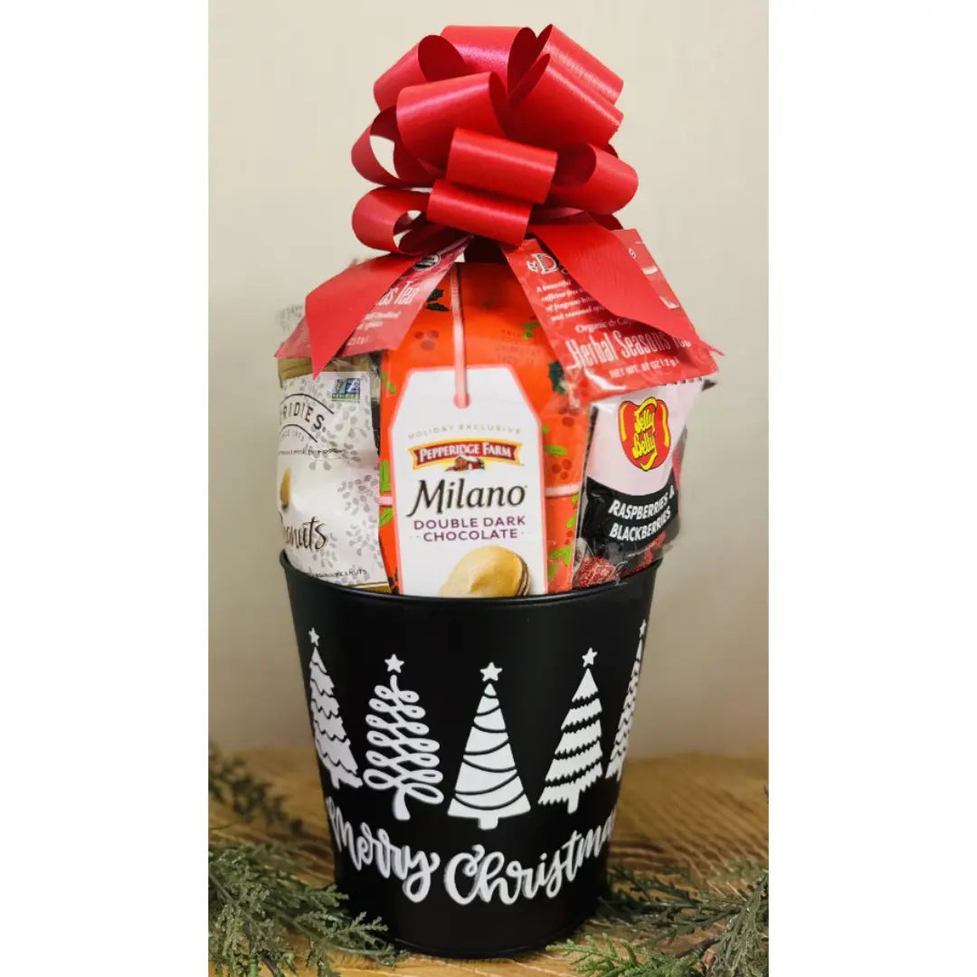 Gift basket with a red bow containing Milano chocolate and other items, placed in a black bucket with Christmas tree designs.